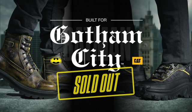 SOLD OUT. Feet wearing Batman x CAT footwear standing on a high ledge overlooking Gotham.